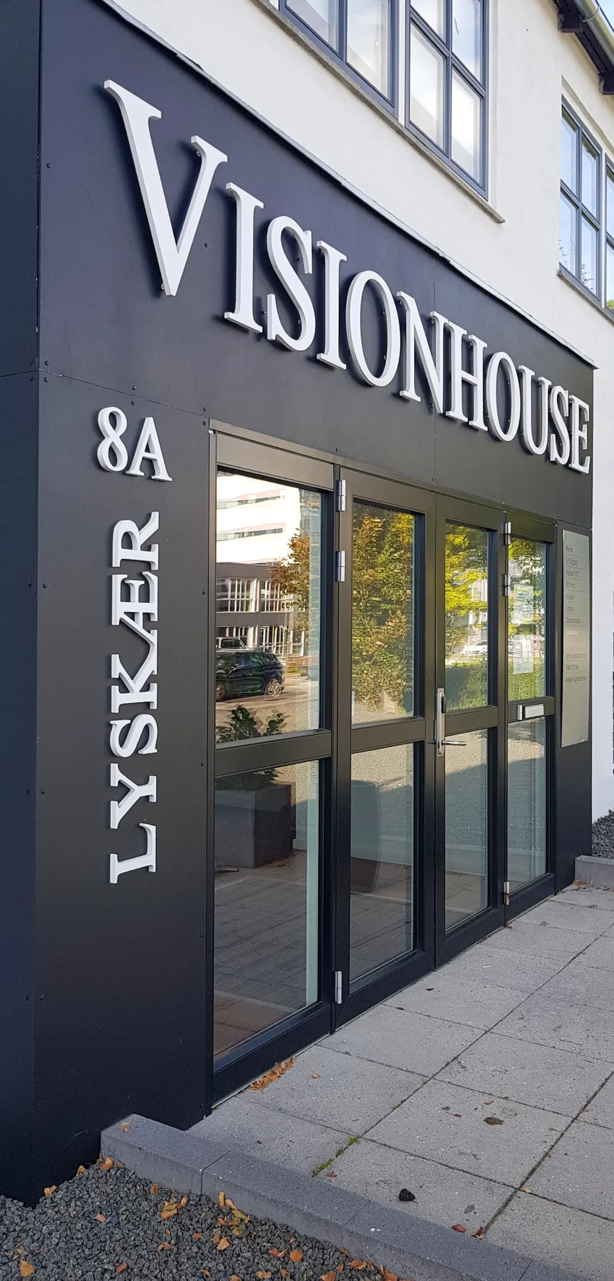 Facadeskilt med Visionhouse i hvide bogstaver på mørk facade