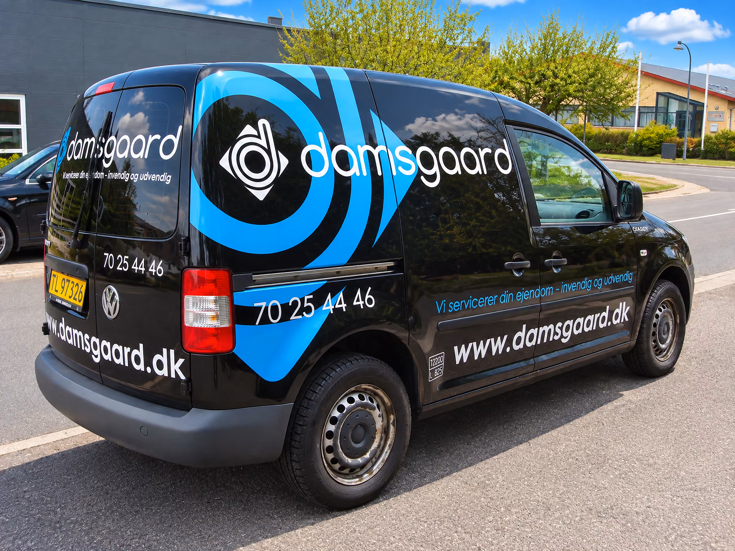 Bilreklame med stort logo og grafik på Damsgaards sorte VW Caddy
