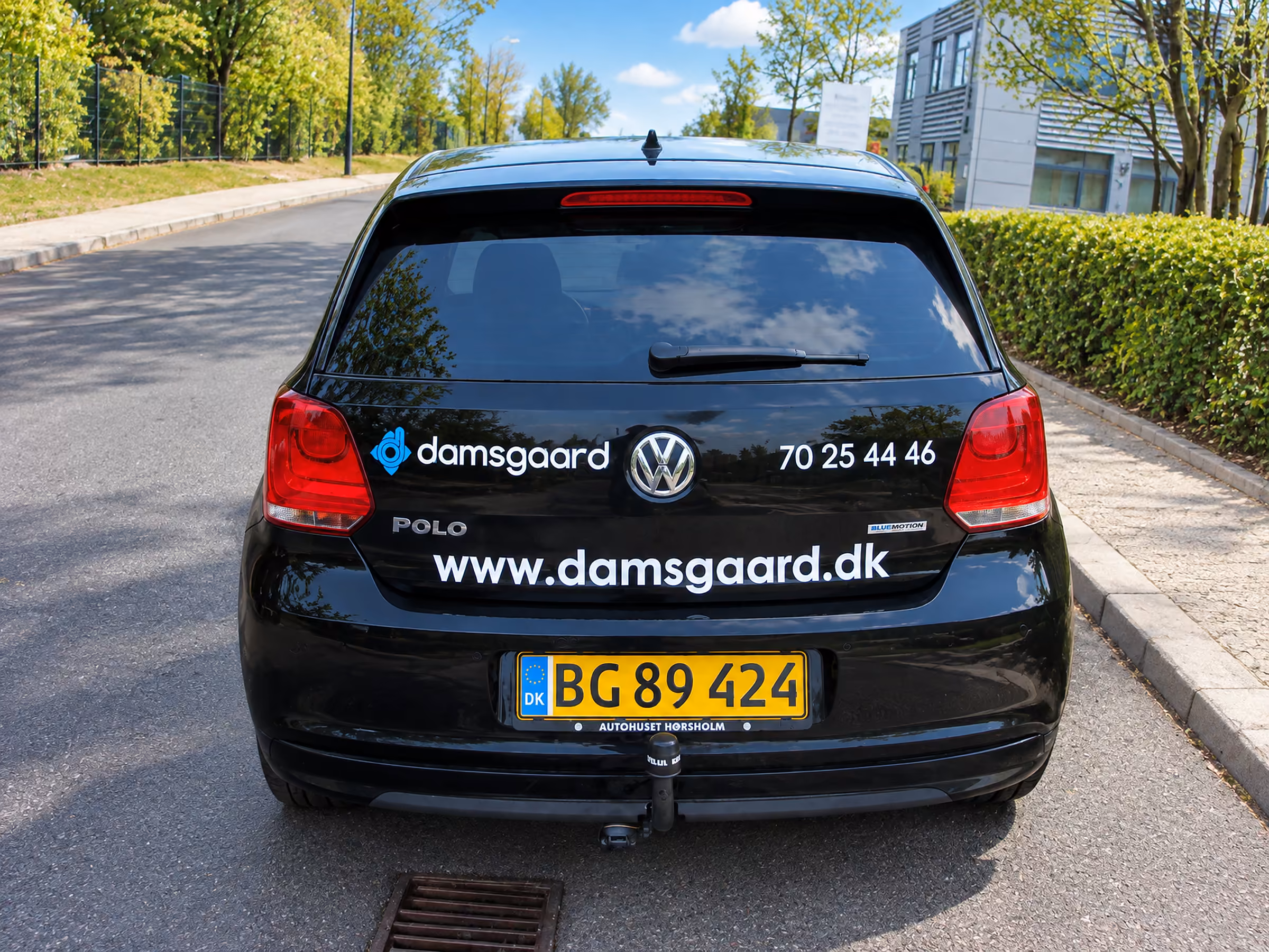 Bagenden af Damsgaards VW Polo med logo, telefonnummer og webadresse