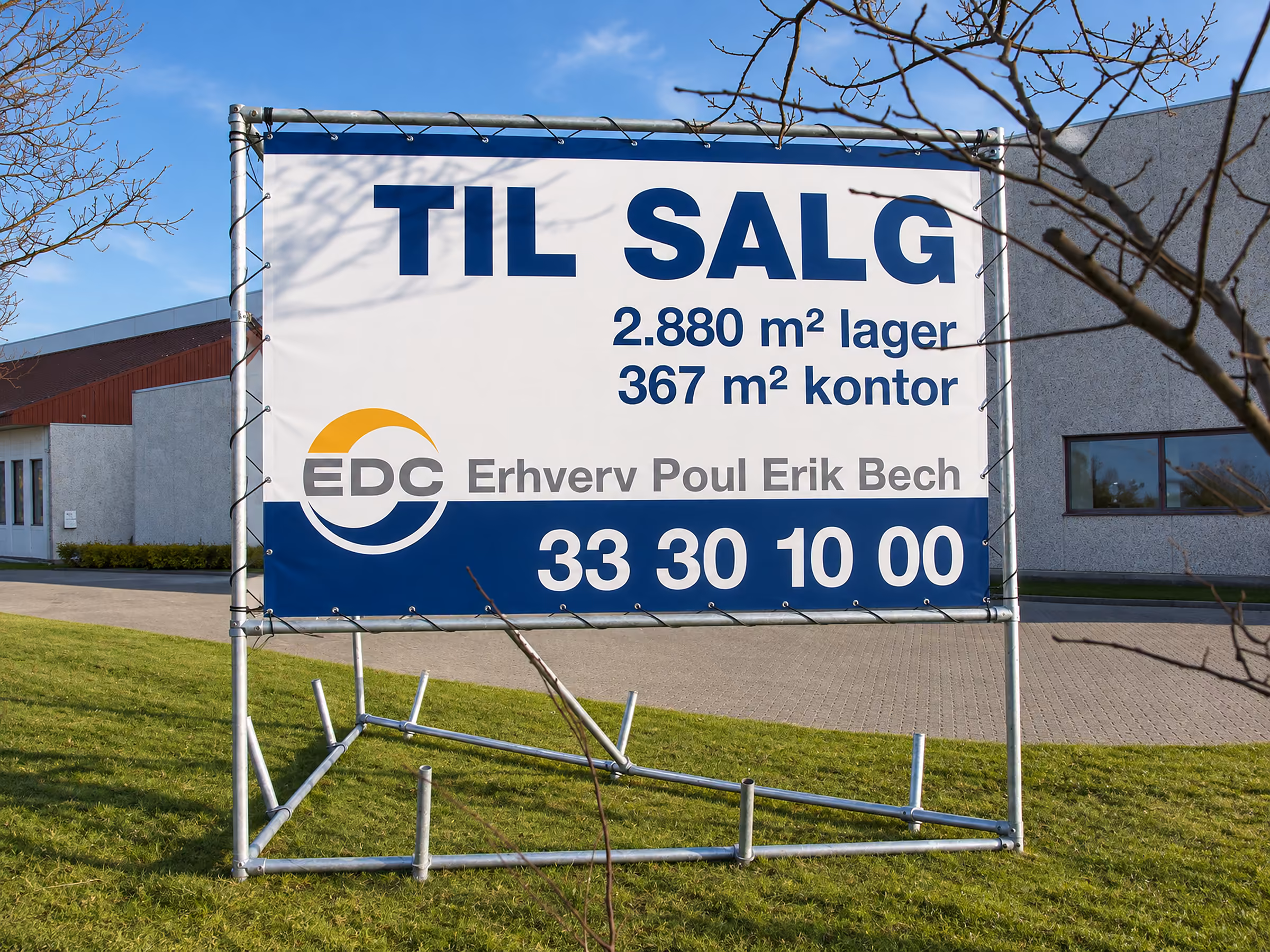 TIL SALG-skilt med lager- og kontorarealer i stativ på en erhvervsgrund