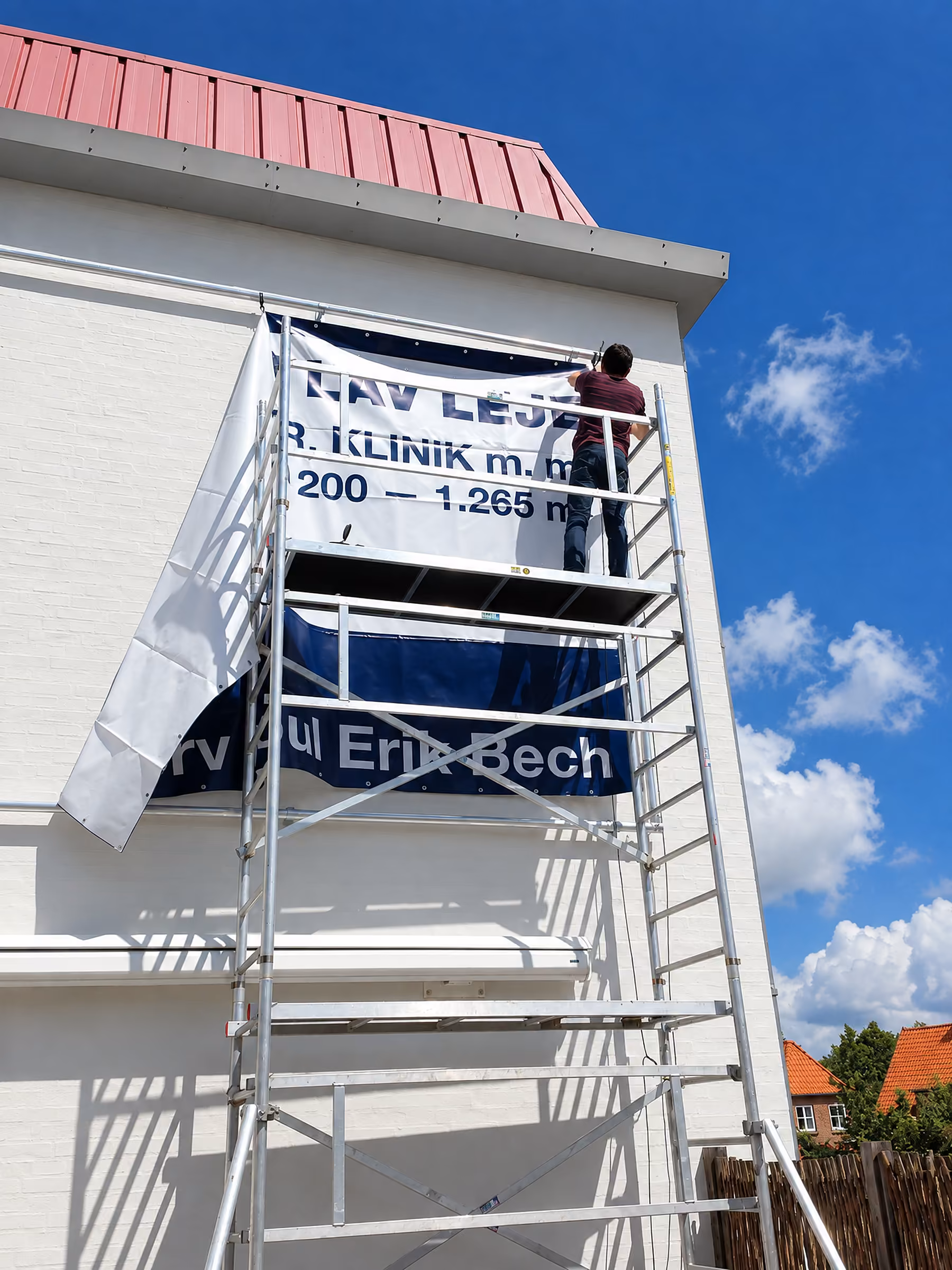 Montør sætter et banner for Erhverv Poul Erik Bech op fra et alustillads