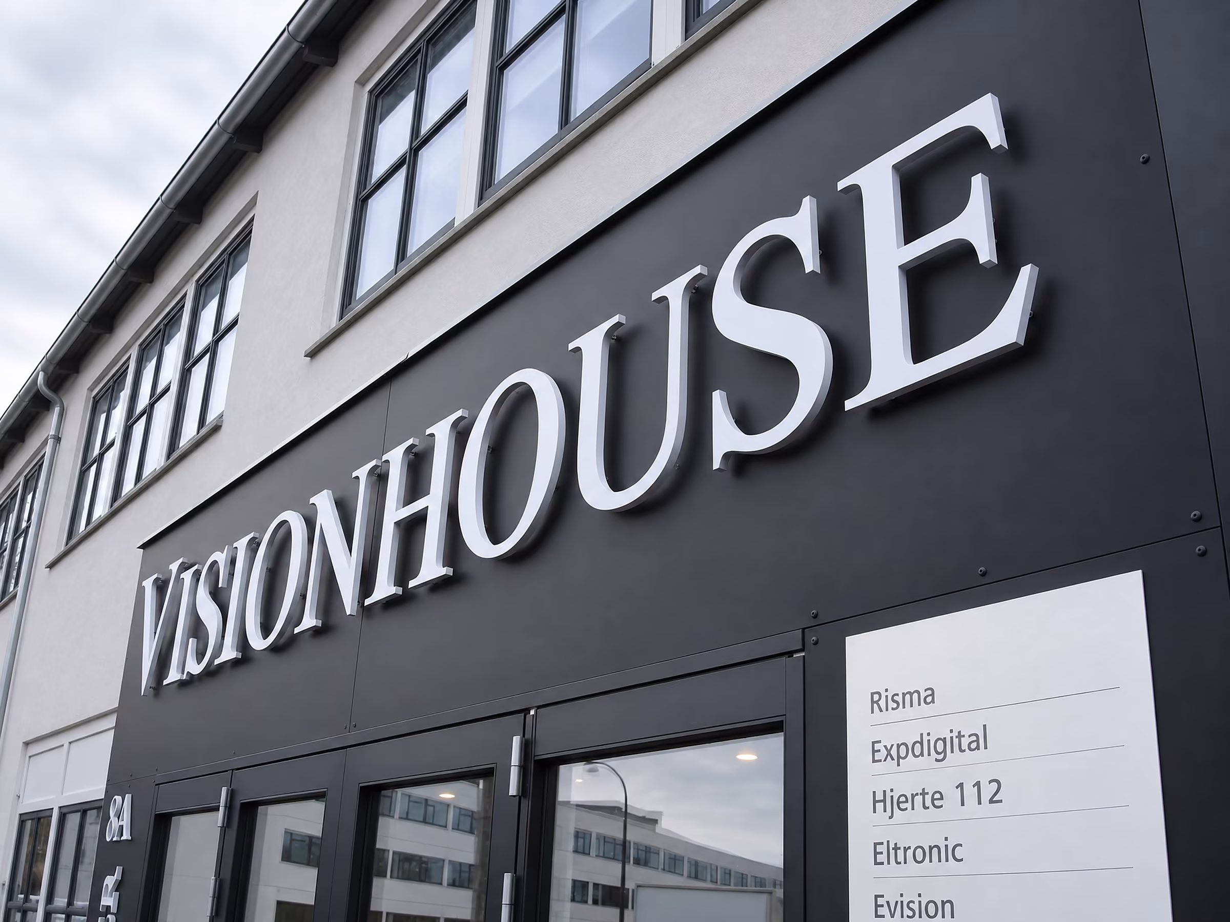 Store hvide 3D-bogstaver VISIONHOUSE på sort facadebånd set nedefra