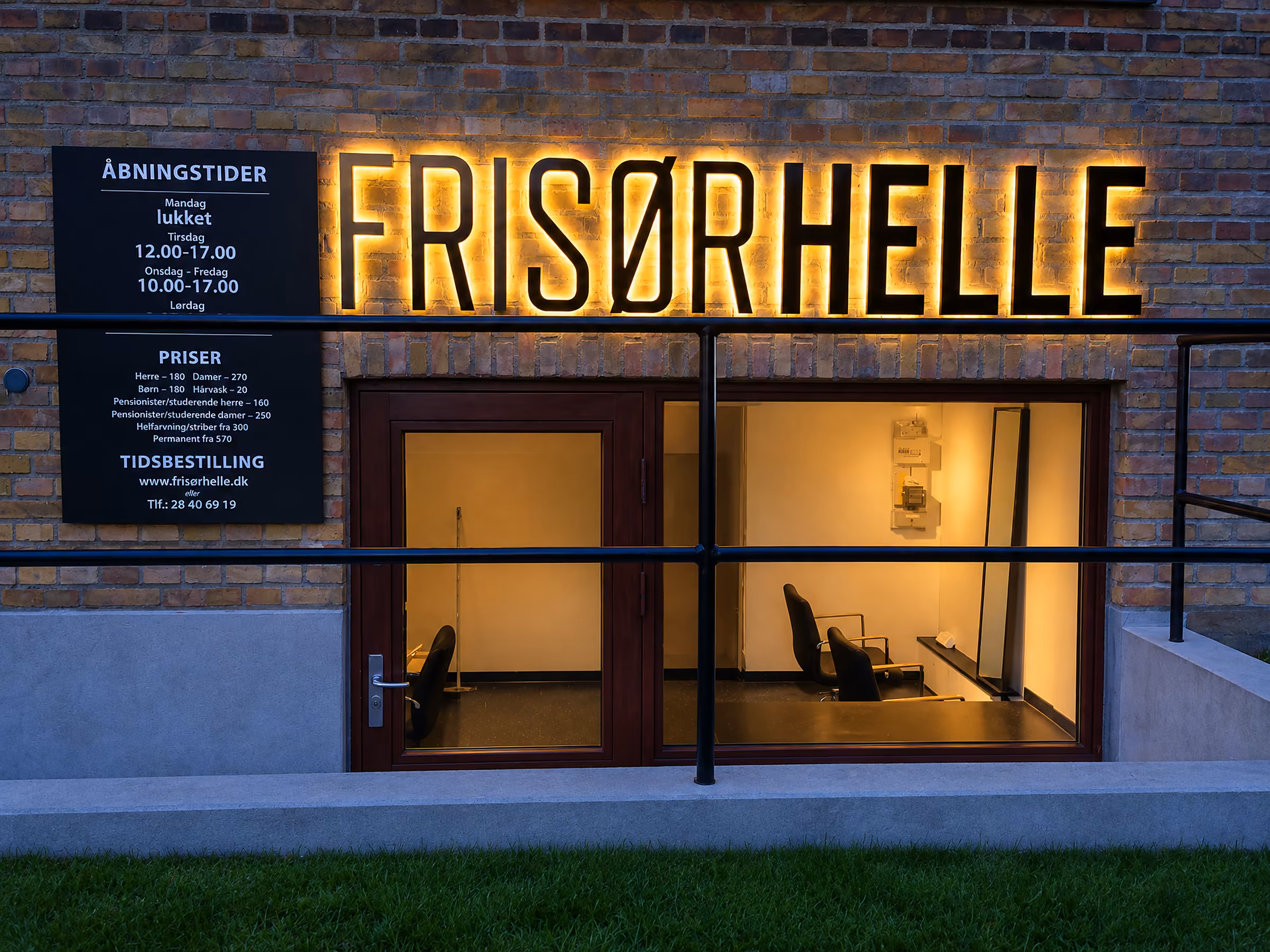 Bagbelyste facadebogstaver på Frisør Helles murstensfacade om aftenen