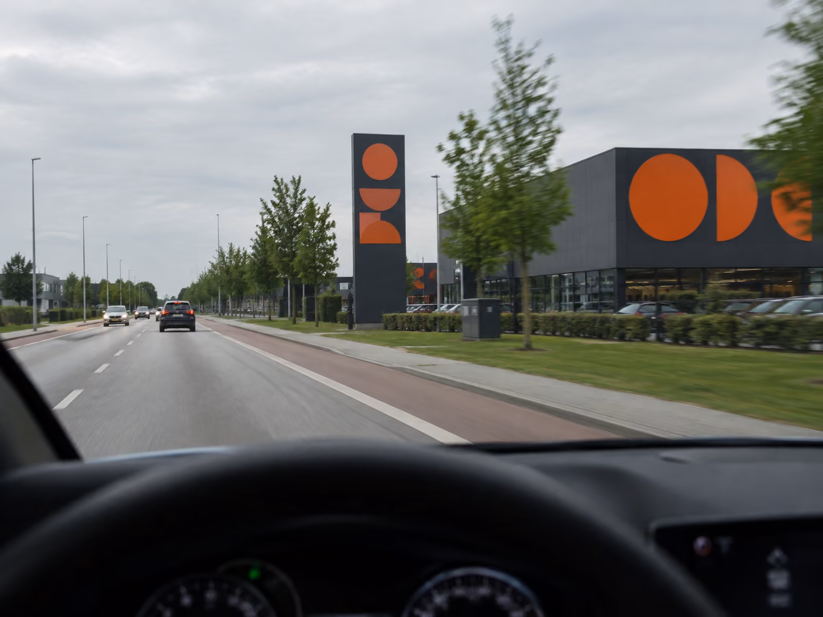 Illustration af facadeskilt og pylon set fra førersædet i en bil på en vej med cykelsti